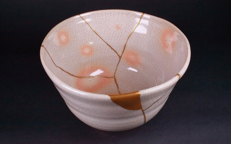 A craftsperson repairing a cracked cup with gold lacquer