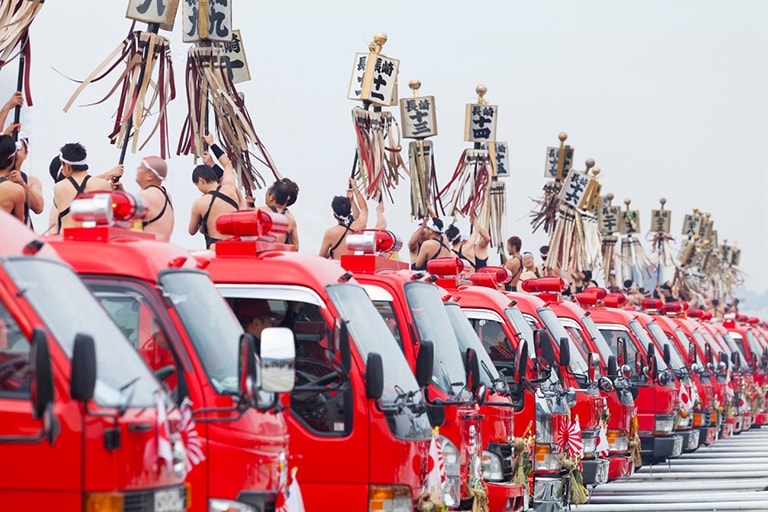 A row of fire trucks with fire fighters all holding traditional banners