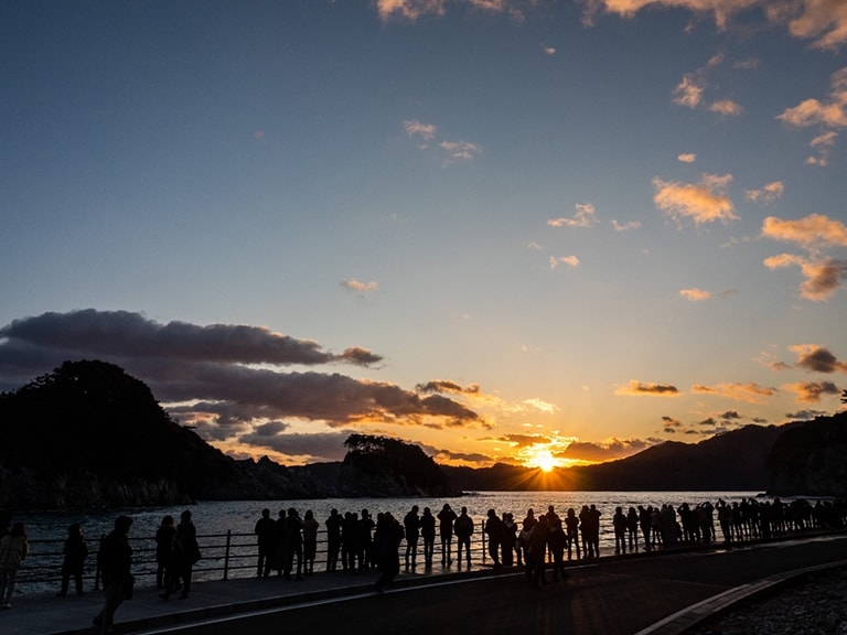 People line up beside a body of water watching the sunrise