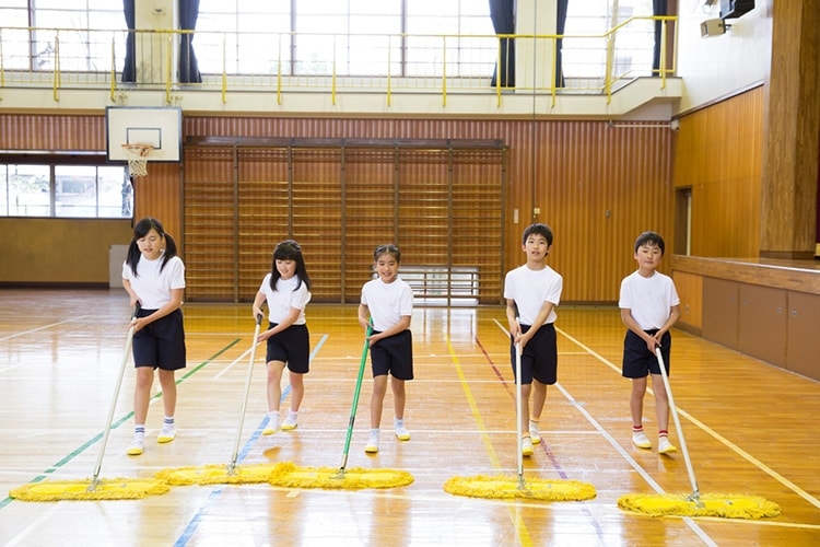 Schoolkids pushing mops across a gymnasium 