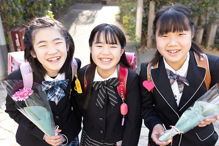 Three schoolkids in Japan holding graduation bouquets