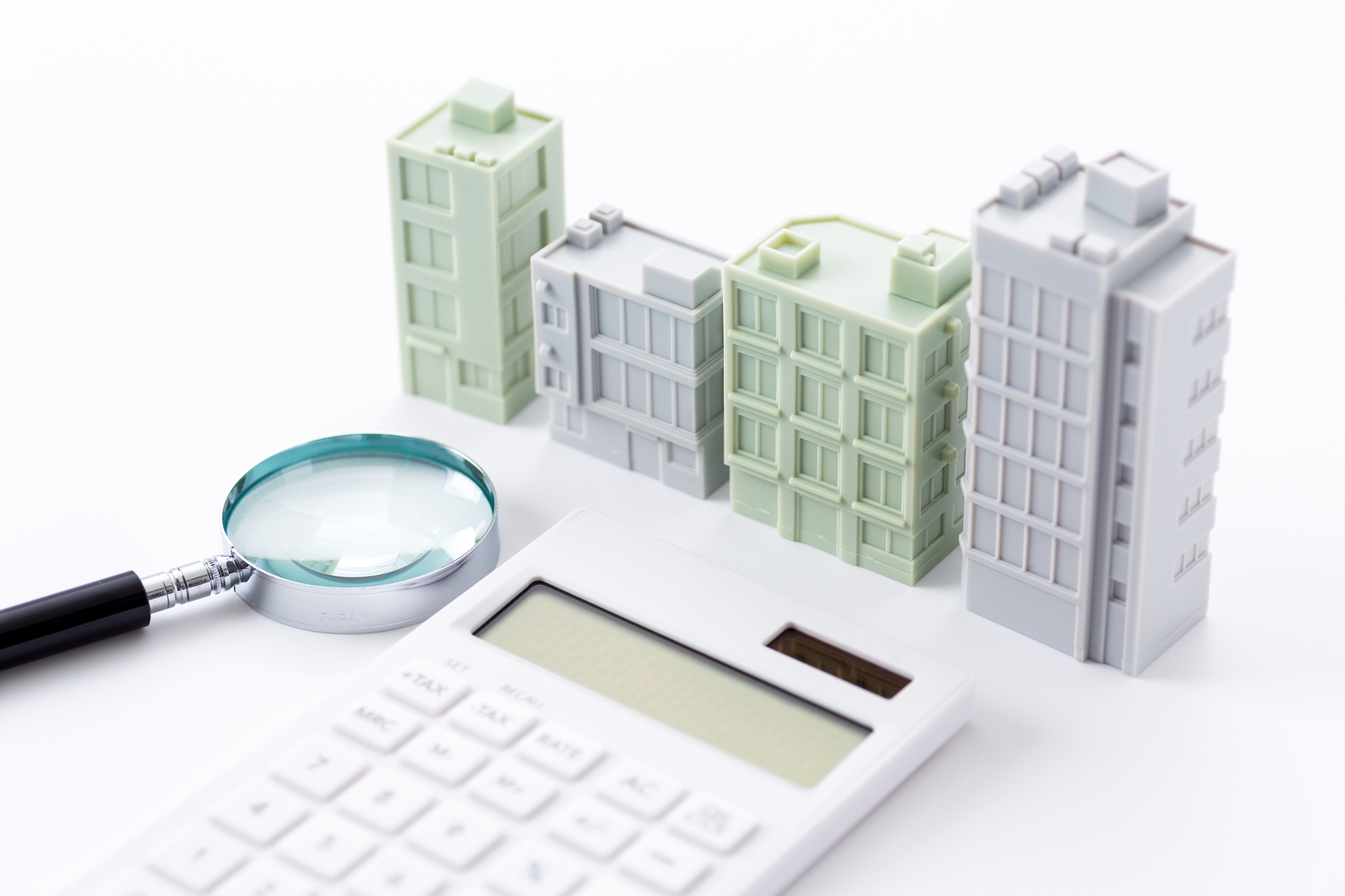 photo of a calculator and a magnifying glass in front of models of office buildings