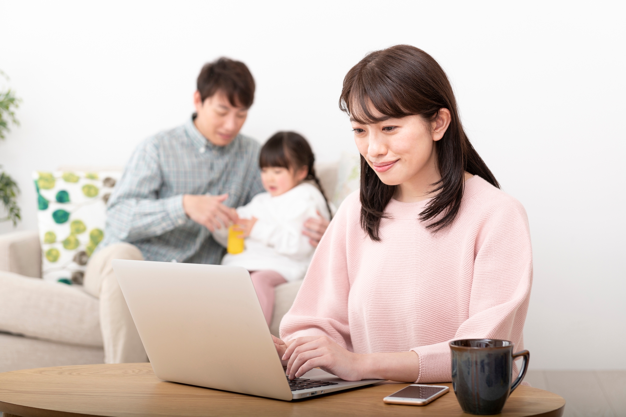 A mother working while her husband cares for their daughter