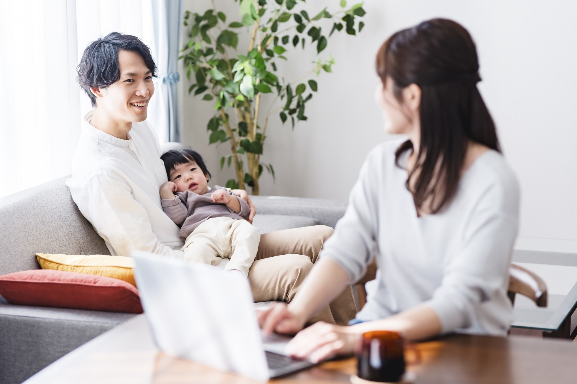 A father sitting with a small child while the mother works on a computer