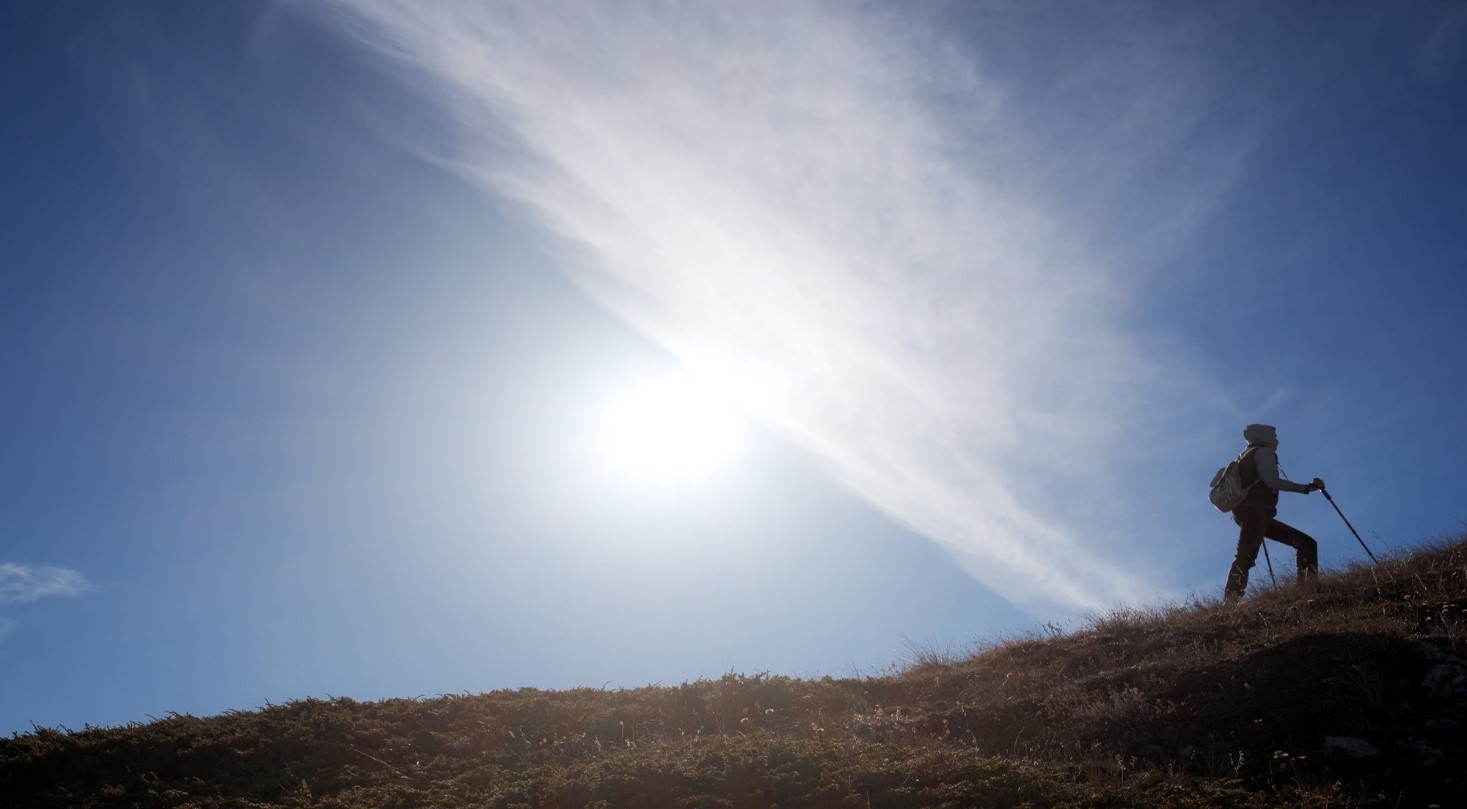 A woman climbing a mountain against a bright blue sky 