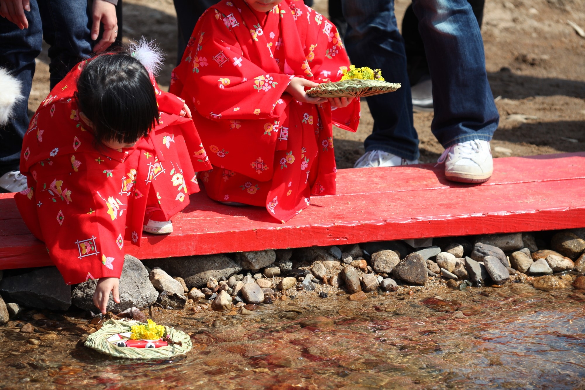 A young girl in kimono placing a straw raft in a river