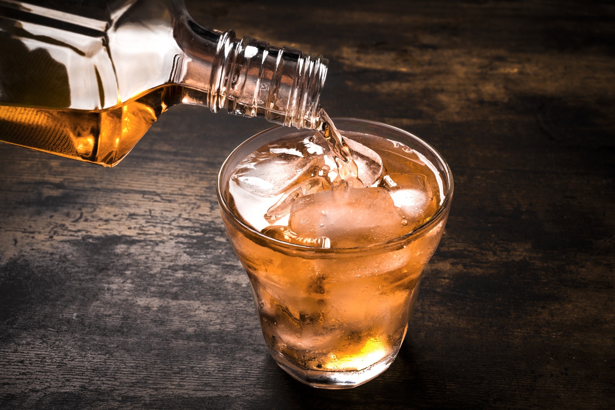 Whiskey being poured into a tumbler with ice