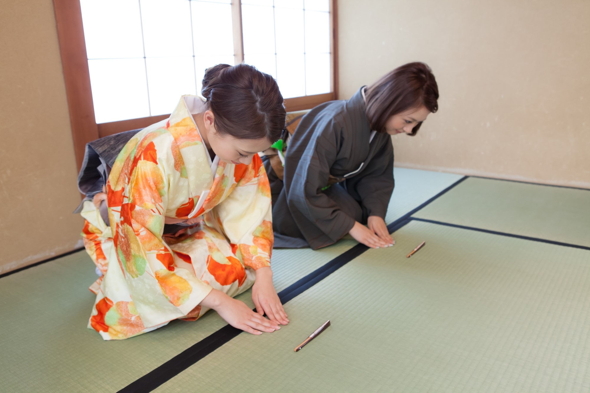 Two women in a Japanese tea ceremony with fans placed in front of their knees as they bow to guests