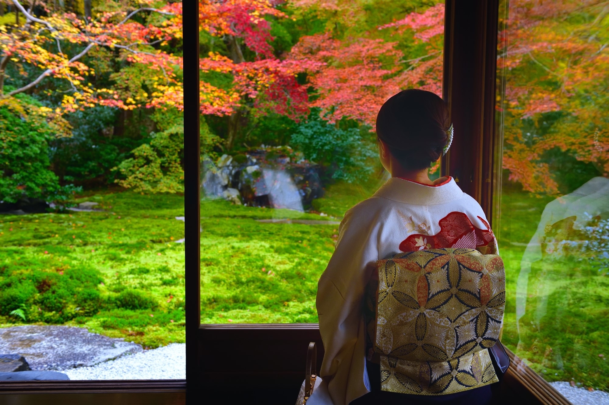 A woman wearing Kimono sitting and looking out into a garden.