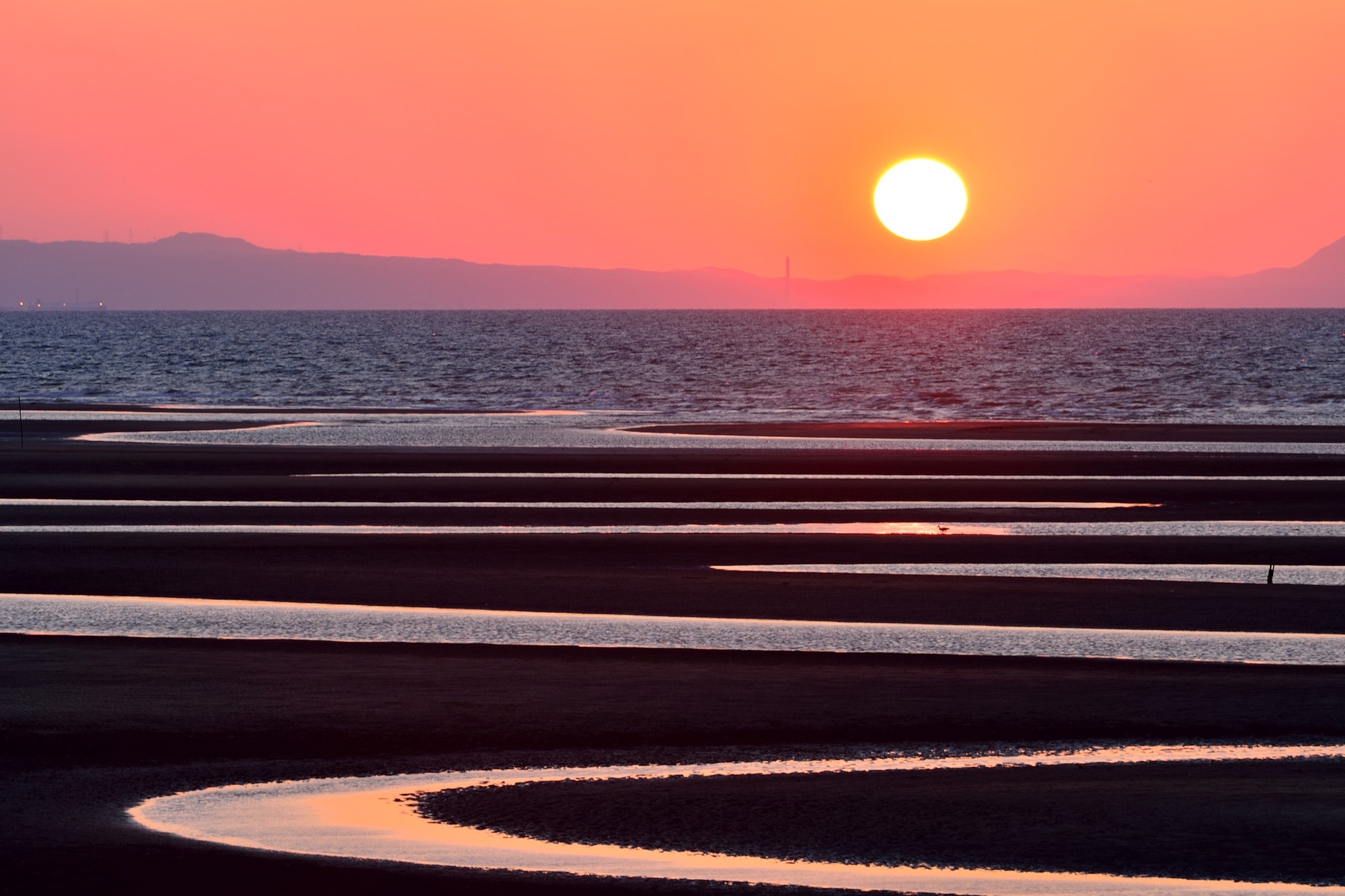 The sun setting into the sea and sandy beach