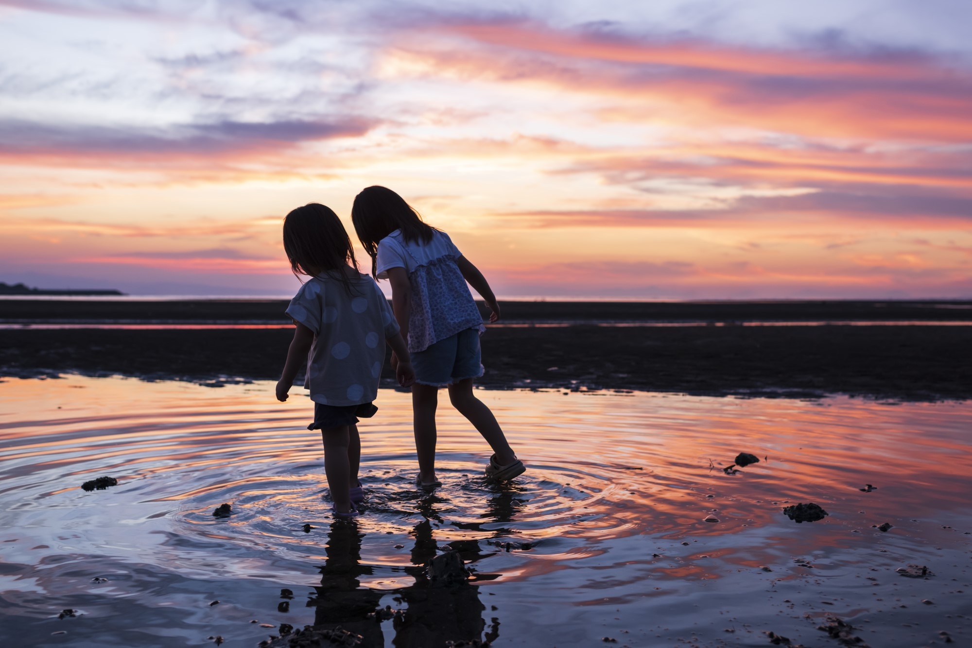 Children enjoying standing on the beach at sunset